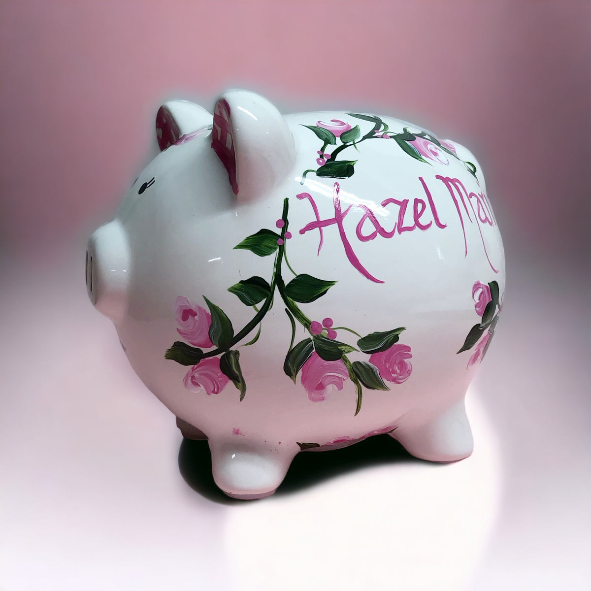 hand painted personalized piggy bank with pink rosebuds and green leaves and vines. A lovely new baby gift.