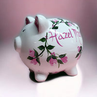 hand painted personalized piggy bank with pink rosebuds and green leaves and vines. A lovely new baby gift.